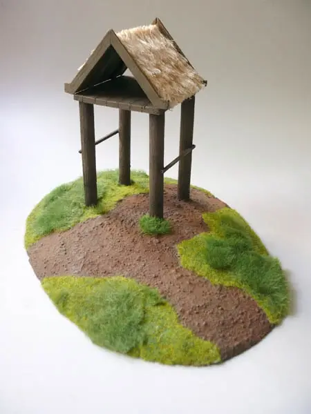 A scenery piece with tall trees on a base covered in brown earth and patches of green grass