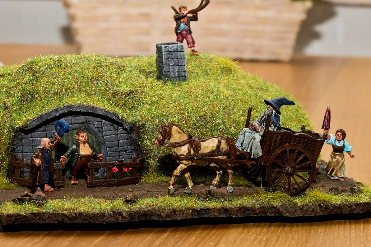 A Middle Earth village diorama with a round door built into a grassy hill and a horse drawn cart