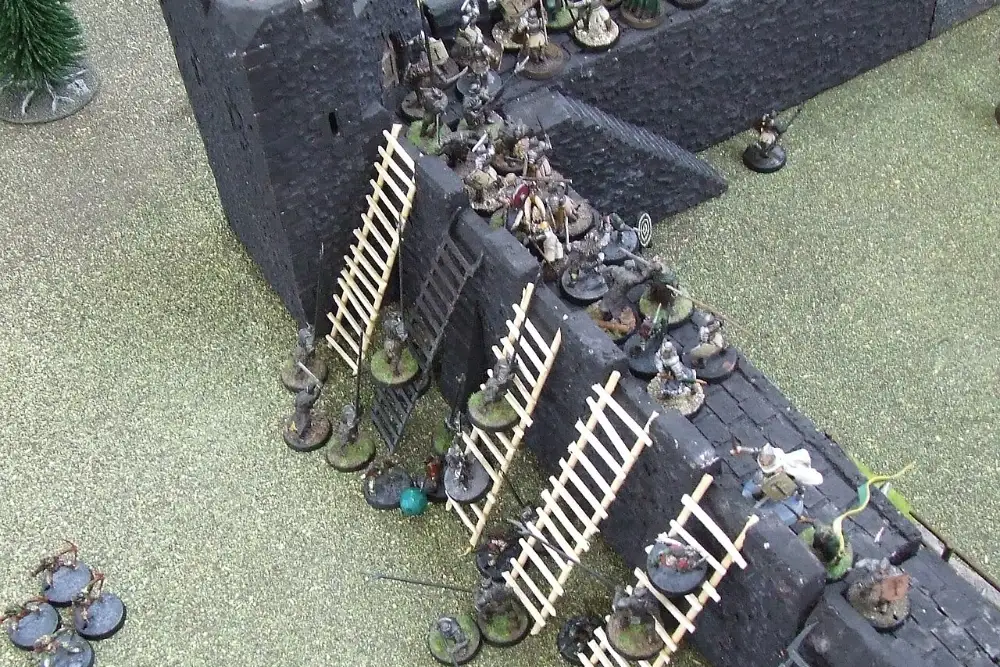 Miniatures climbing ladders up a fortress wall during a Middle Earth battle